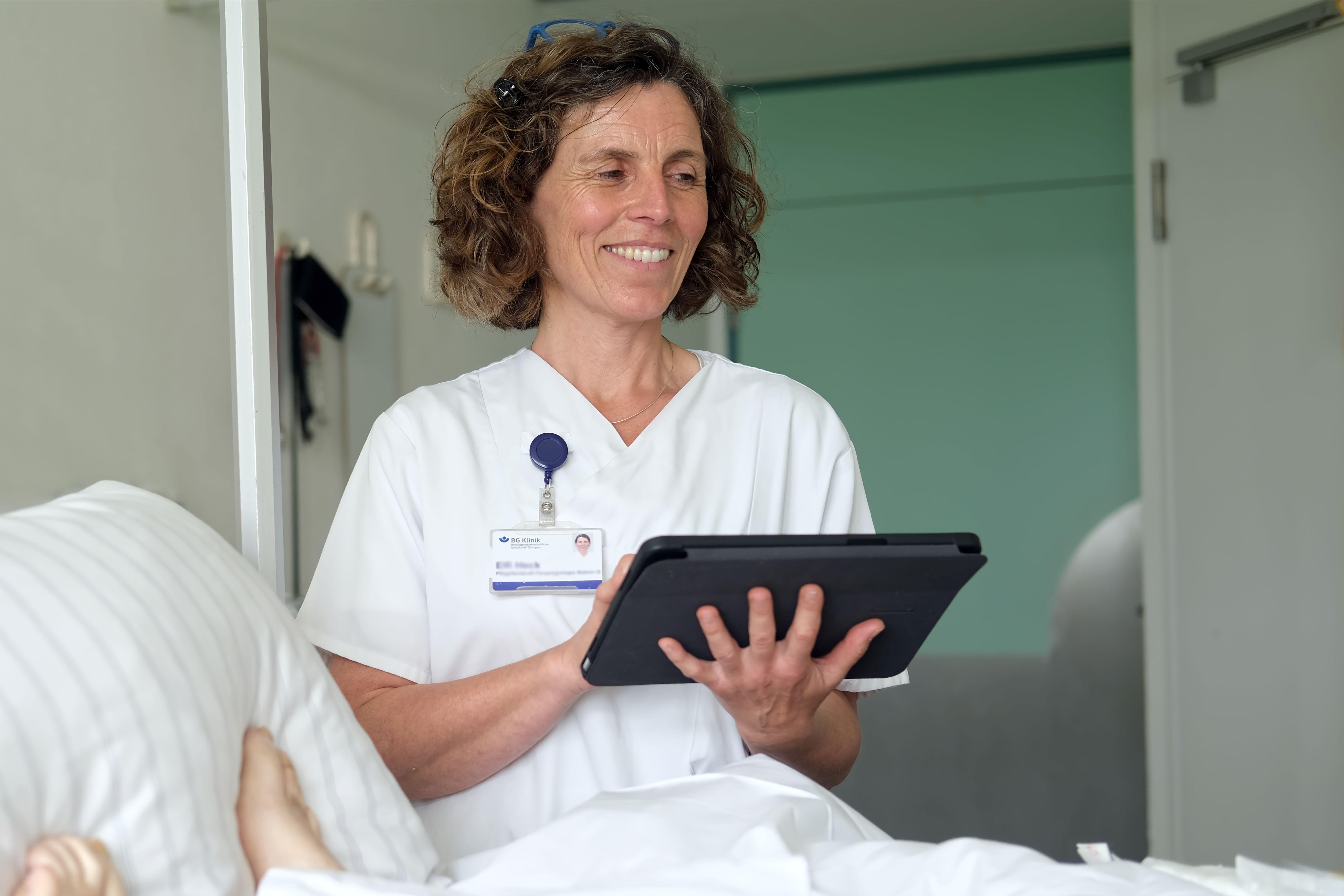 Pflegefachkraft mit Tablet am Patientenbett.