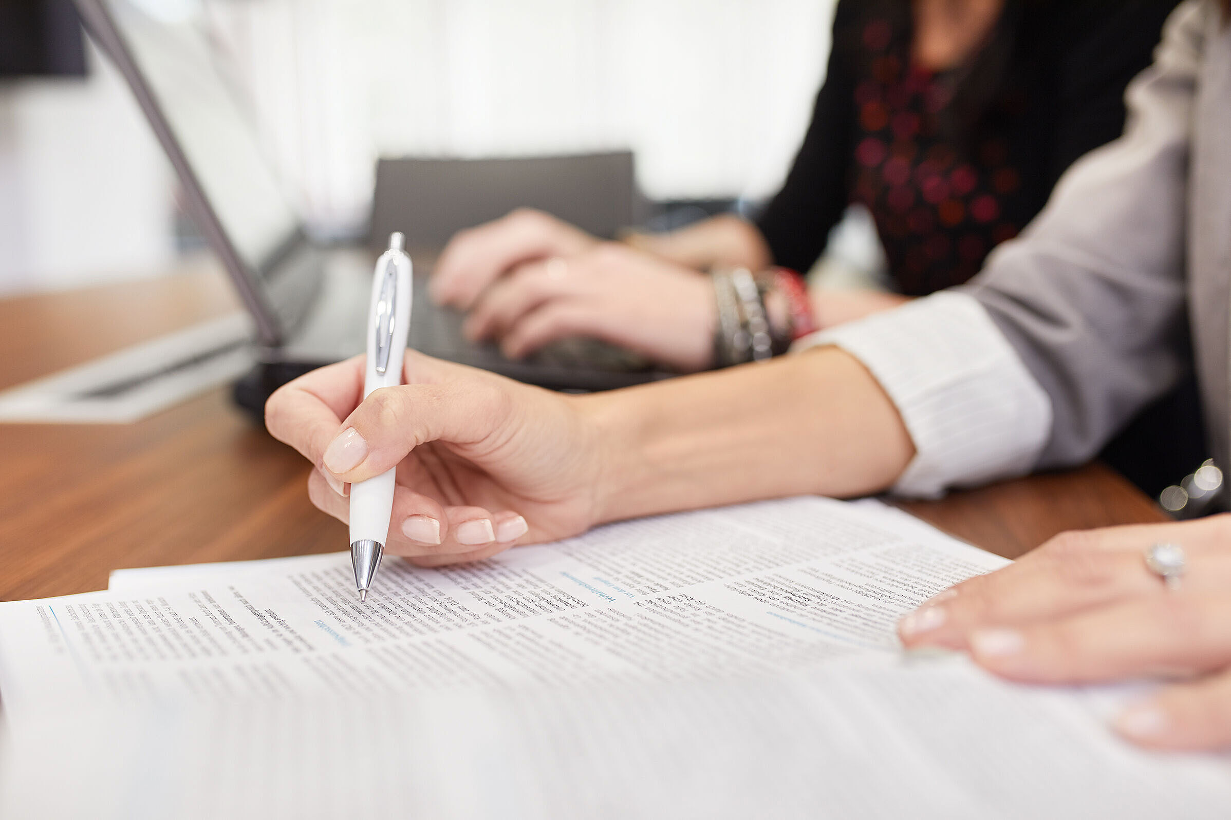 Die Hände zweier Frauen vor einem Blatt Papier und Computer