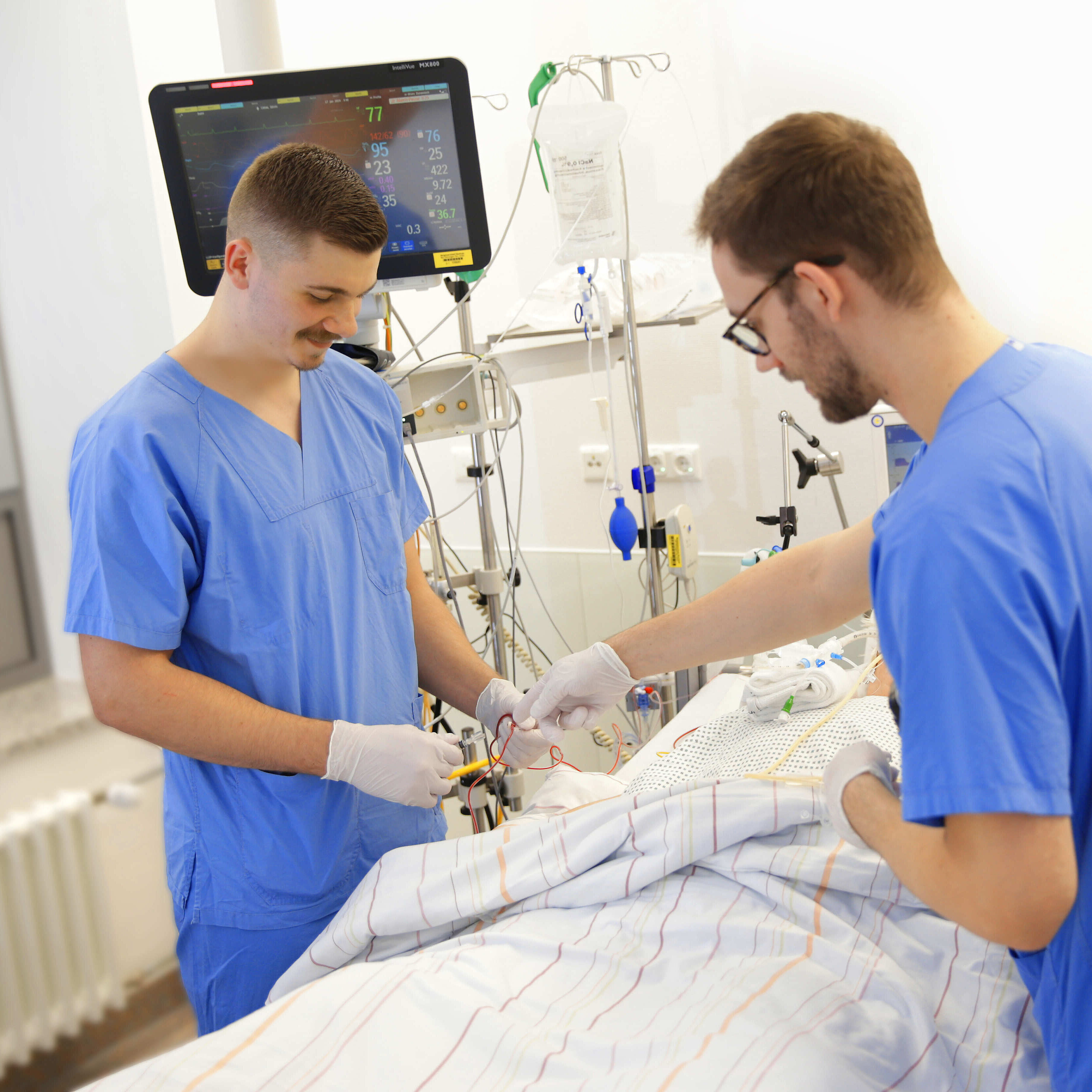 PflegePlus: Unser neues Ausbildungskonzept zur Pflegefachkraft mit Schwerpunkt Intensivpflege und Anästhesie. Bild: Pflegefachkraft und Auszubildender in einer Simulationsanleitung am Intensivbett.