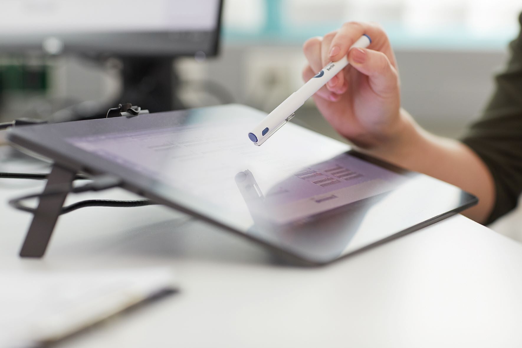 Hand mit Kugelschreiber zeigt auf Tablet