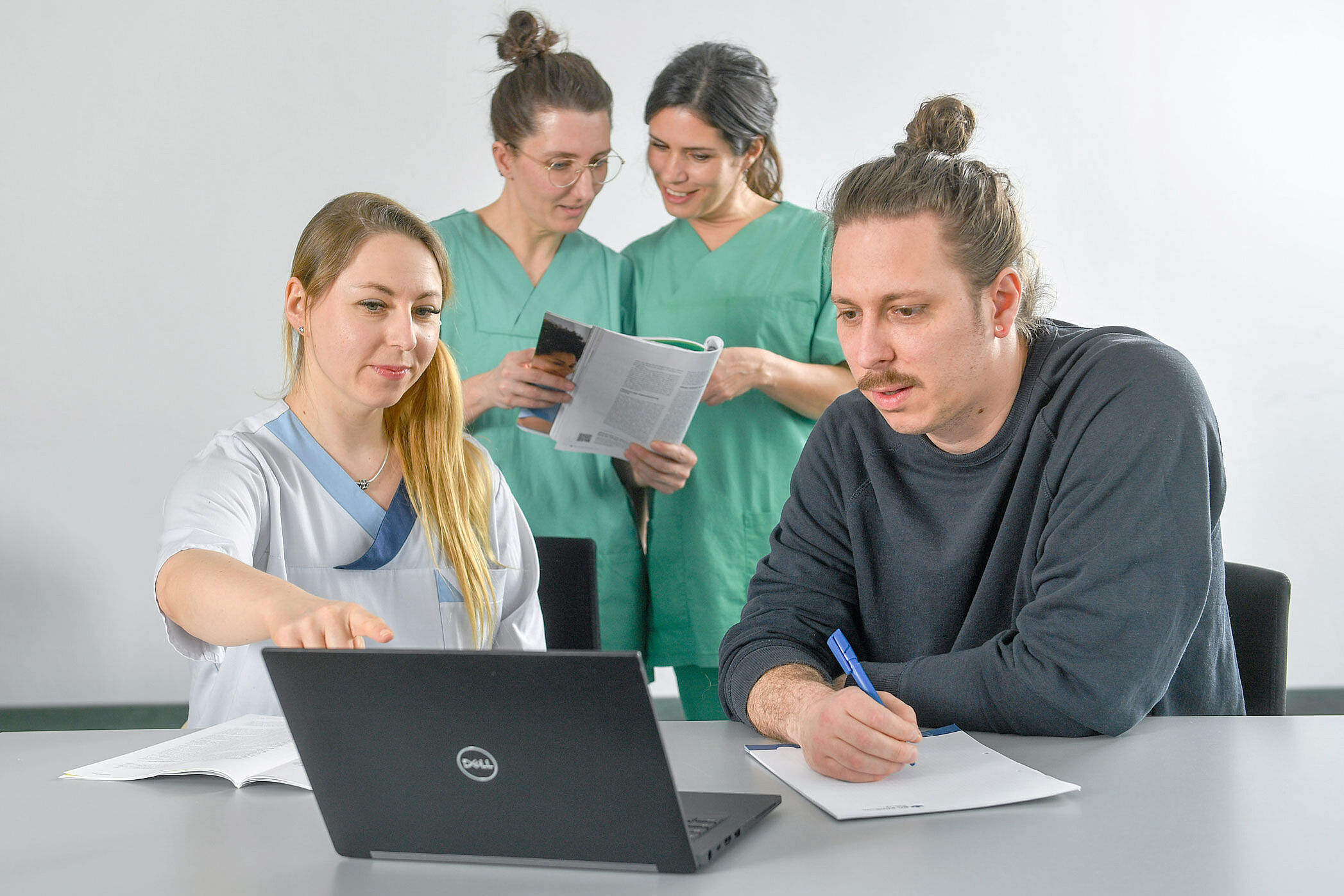 Vier Personen in Teamarbeit: zwei stehend im Hintergrund, zwei vorne sitzend am Laptop