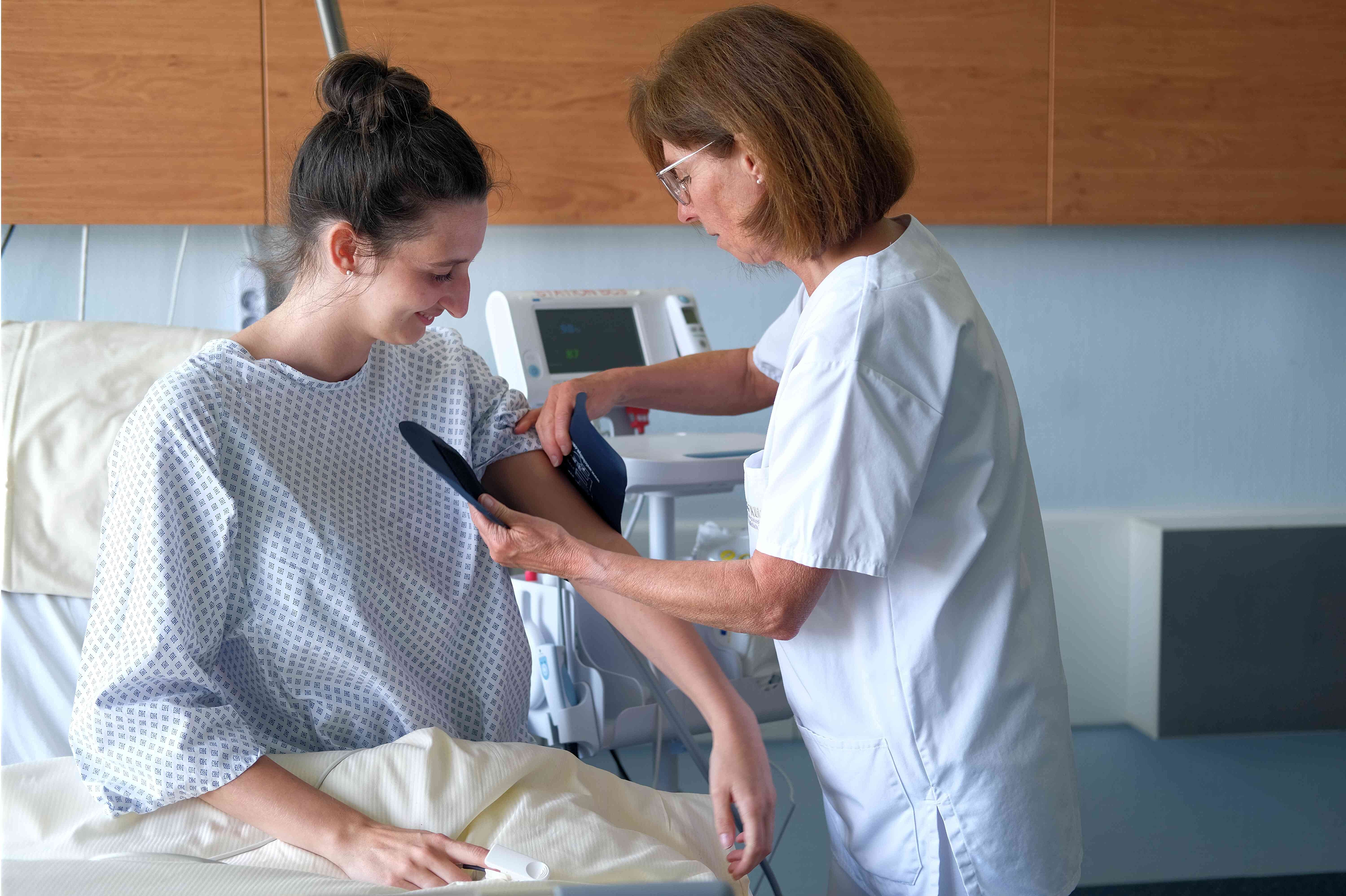 Pflegekrat beim Blutdruckmessen an Patientenbett.