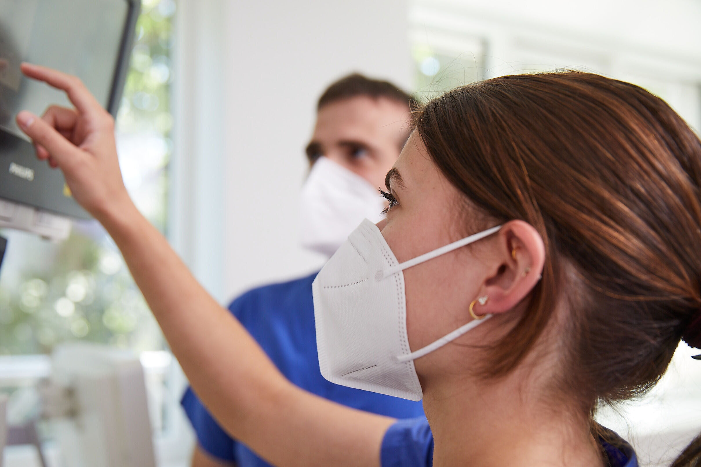 Frau mit Maske zeigt auf Monitor